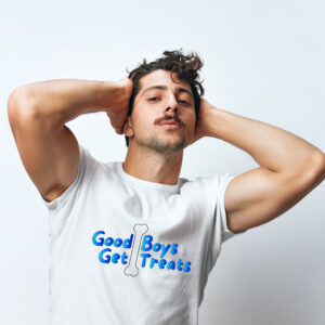 A man stands confidently against a plain background, wearing the "Good Boys Get Treats" white t-shirt featuring a playful bone graphic, with his hands resting casually on his head.