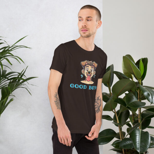 A man wearing a Good Boy T-shirt featuring a cartoon dog and text, standing next to indoor plants.