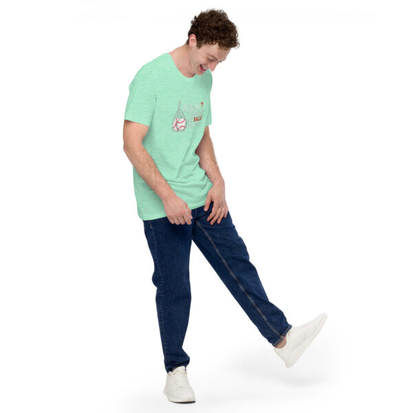 Wearing a "Really?! I washed my balls for this!" green T-shirt and blue jeans, a person balances on one leg while looking down and smiling against a white background.