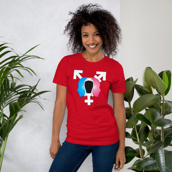 A person smiling, wearing the "Beyond the Binary" red T-shirt featuring a graphic of silhouettes and gender symbols, stands beside green plants.