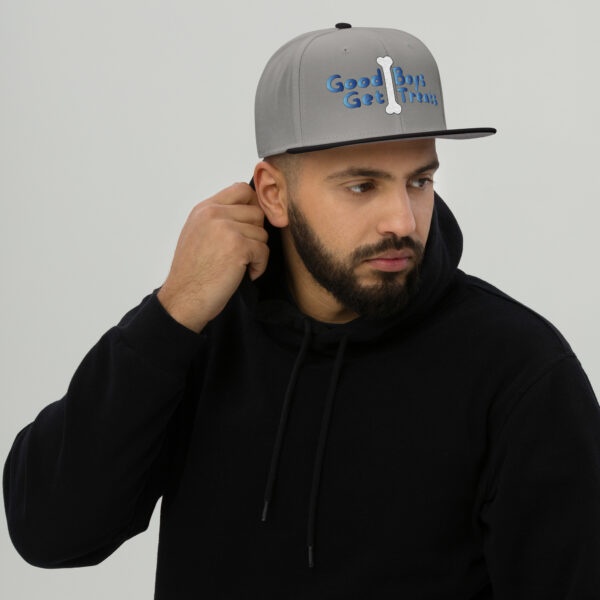 A man sporting a Snapback Hat featuring blue text and a dog bone graphic, paired with a black hoodie, gazes off to the side.