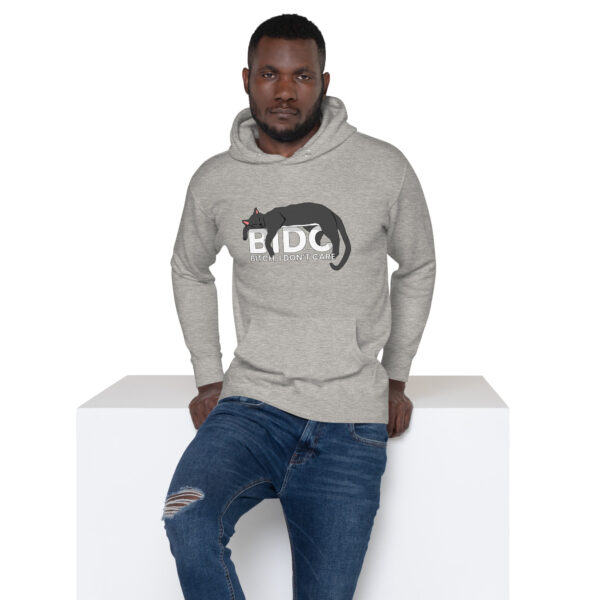 A person wearing the BIDC Hoodie, which features a graphic of a black cat and text, is leaning on a white surface while wearing ripped jeans.