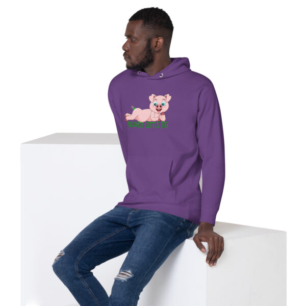 A man wearing the Naughty Little Pig Hoodie with a cartoon pig design sits on a white block.