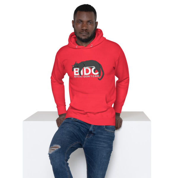 A man wearing the BIDC Hoodie, featuring a red design with a cat graphic and text, is leaning against a white surface.