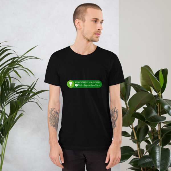 In a room filled with green plants, a person wears the "Achievement: Gaymer Boyfriend" black t-shirt.