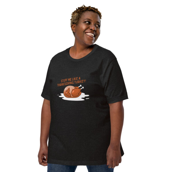 A person wearing the "Stuff Me" T-shirt, featuring a black fabric with a roasted turkey graphic and the text "Stuff me like a Thanksgiving turkey!", smiles and looks to the side.