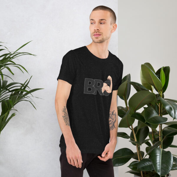 A man in a black Bro t-shirt featuring the word "BRO" and a flexed bicep graphic stands near a wall and potted plants.