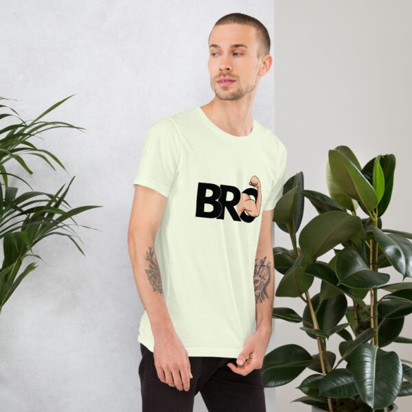 A man stands near green plants wearing a light t-shirt featuring the "Bro" design with a fist graphic.