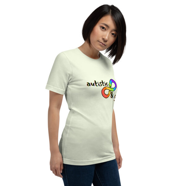 A person wearing a light-colored T-shirt featuring the rainbow infinity symbol alongside the phrase "Autistic & Gay.