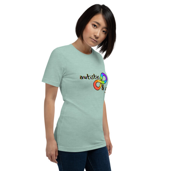 A person wearing an "Autistic & Gay" light green t-shirt featuring a rainbow infinity symbol and the word "autistic" on the front.