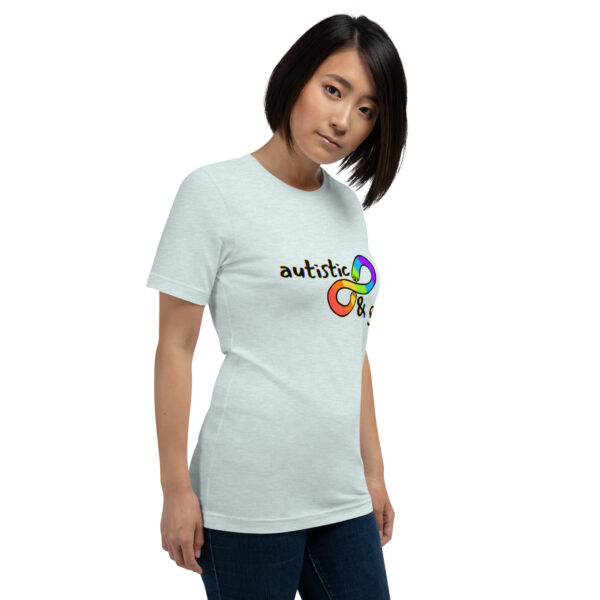 A person wearing a light grey "Autistic & Gay" T-shirt featuring a colorful infinity symbol.