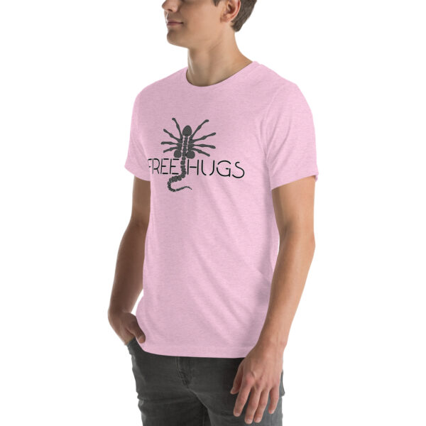 A person wearing a "Free Hugs" t-shirt in pink, featuring a scorpion graphic, is standing against a plain background.