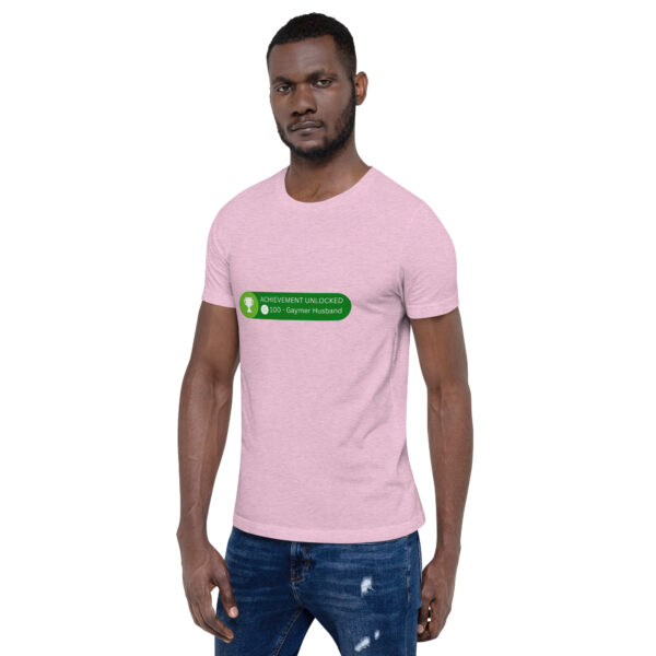 A man wearing the light pink "Achievement: Gaymer Husband" t-shirt featuring green text that reads "ACHIEVEMENT UNLOCKED - 100G - Gaymer Husband.