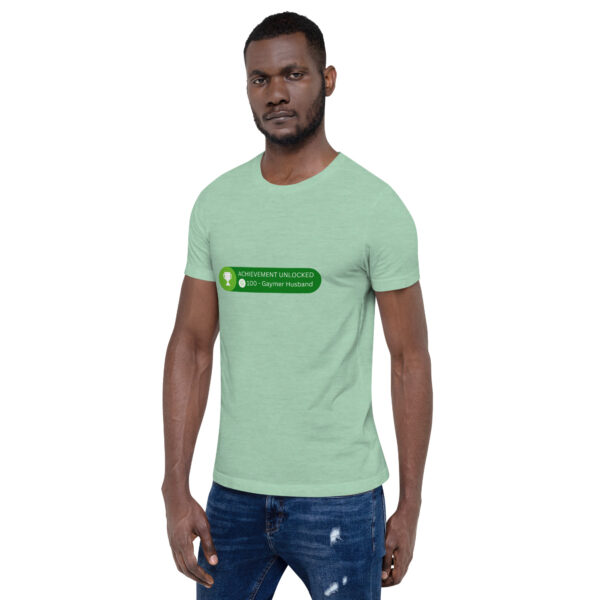 A man wearing the "Achievement: Gaymer Husband" t-shirt in green, paired with blue distressed jeans.