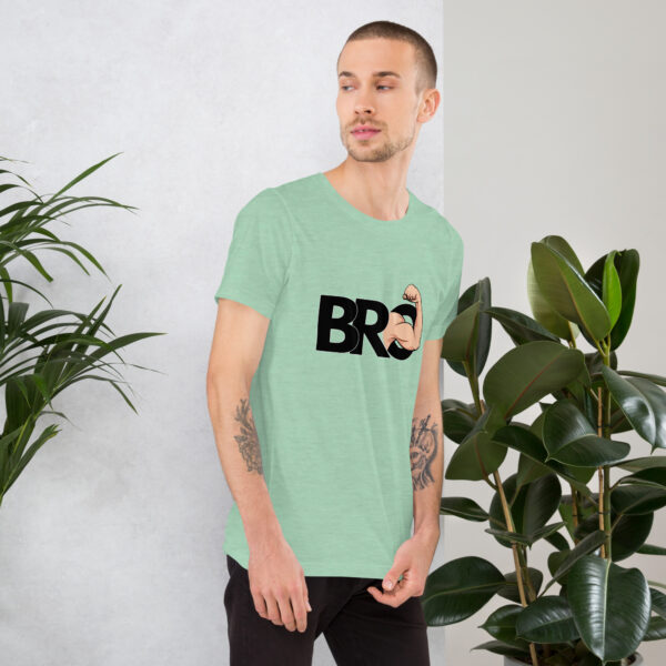 Man wearing a light green "Bro" T-shirt, standing next to green plants, gazing to his left.