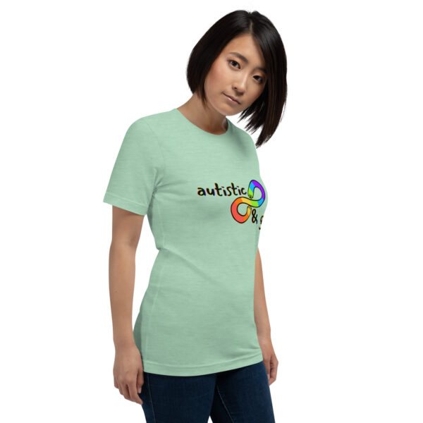 A person wearing the "Autistic & Gay" light green t-shirt, featuring the word "autistic" and a colorful infinity symbol, stands against a plain background.