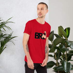 A man wearing a red "Bro" shirt stands near green plants, gazing to his left.