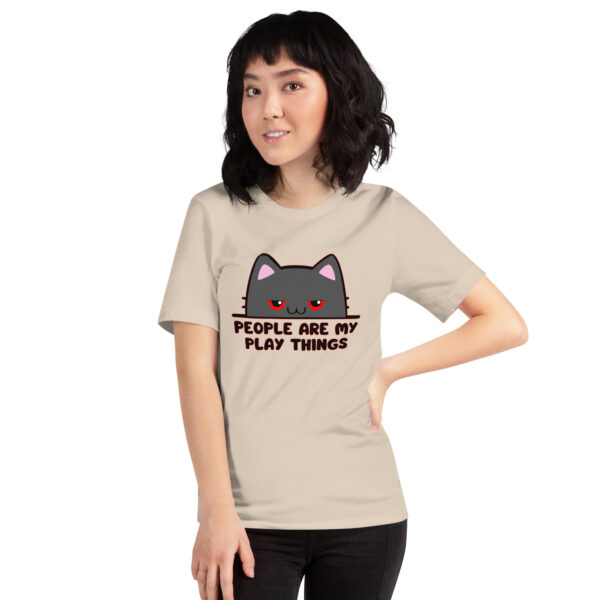 An individual wearing a beige T-shirt featuring a cartoon cat and the phrase from the "People Are My Play Things" product line.