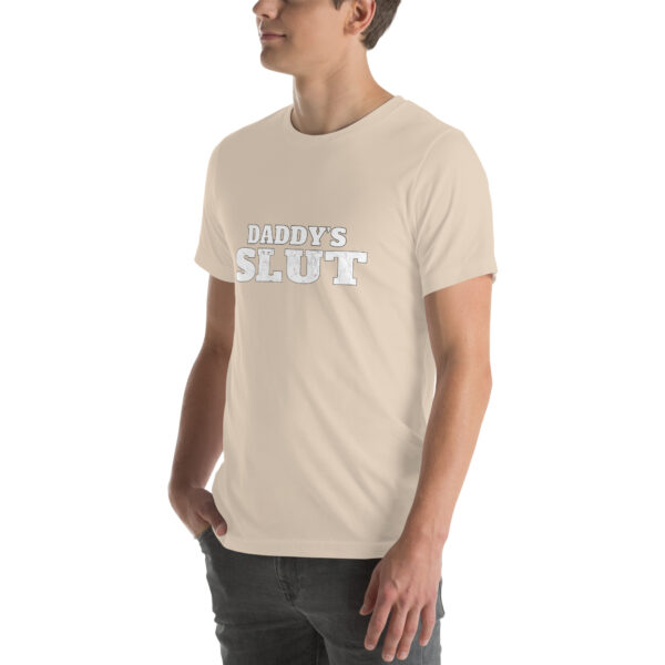 A person wearing a beige t-shirt featuring bold white text "Daddy's Slut" on the front.