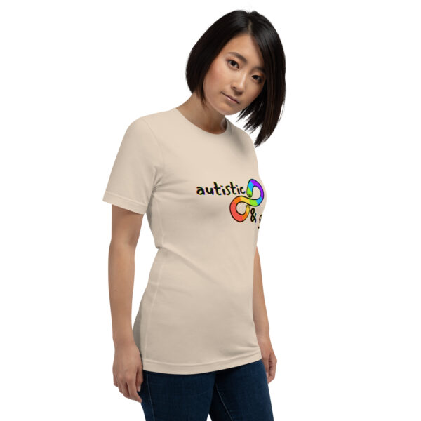 Person wearing a beige T-shirt adorned with a colorful infinity symbol and the phrase "Autistic & Gay.