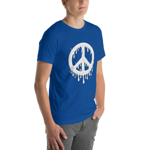 A person wearing the "Cum in Peace" blue t-shirt featuring a white, drippy peace symbol design, with their hands in pockets and paired with gray jeans.