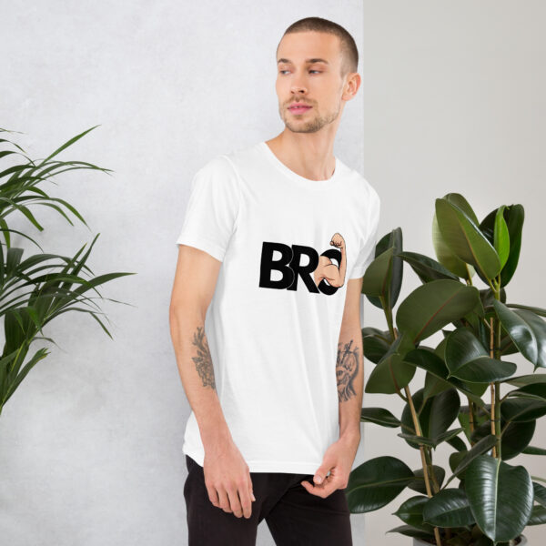 A person with short hair and tattoos is wearing a white T-shirt featuring the "Bro" design, standing next to potted plants in a bright room.