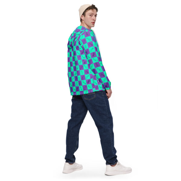 A person sports a jacket featuring the Checkered Drawn Penis Pattern in teal and purple squares, paired with dark jeans, white sneakers, and a beige beanie. They glance over their shoulder against a crisp white background.