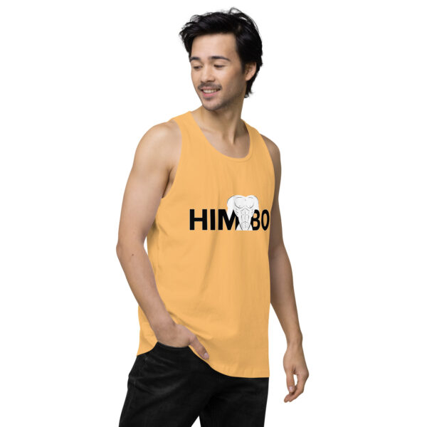 A man in a yellow Himbo Tank featuring an elephant design stands with one hand in his pocket, looking to the side.