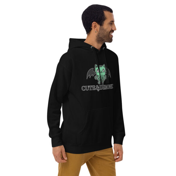 A person wearing the Cute and Demonic Hoodie, featuring a design of a green creature with text, standing sideways.