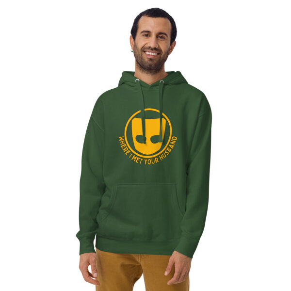 A man stands smiling in a green Where I Met Your Husband hoodie, featuring a yellow emblem and text.