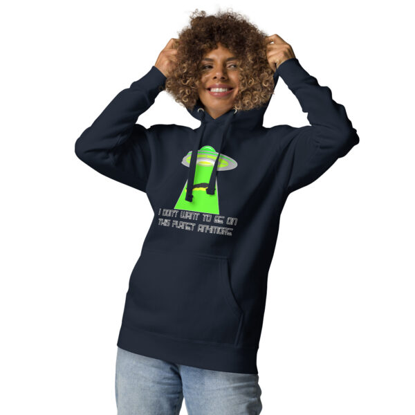 A person wearing the "I don't want to be on this planet anymore" hoodie, featuring a neon green alien design and text about trips to other planets, is smiling and adjusting their curly hair.