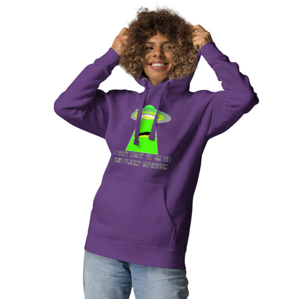 A person wearing the "I Don’t Want to Be on This Planet Anymore" hoodie, which is purple featuring a UFO graphic and text, adjusts the hood while smiling against a white background.