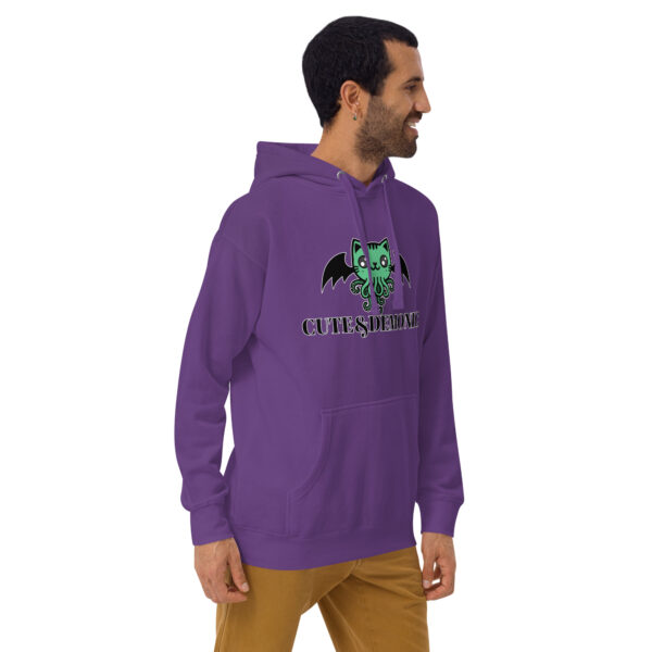 A man is standing and smiling while wearing the "Cute and Demonic Hoodie," which features a purple design with a green cartoon creature and the text "CUTE $ DEMONIC.