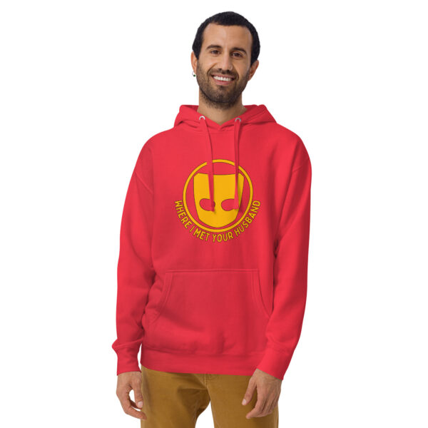 Person wearing a Where I Met Your Husband hoodie, red with a yellow design and text, smiling with hands by sides.