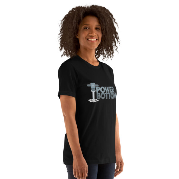 A person is smiling and standing against a white background while wearing the "Power Bottom" black T-shirt featuring a graphic and text.