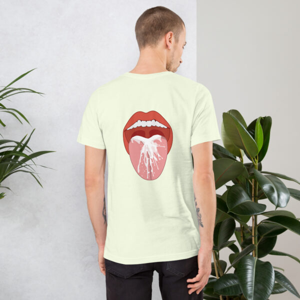 A person with short hair and tattoos is wearing a light-colored Thirsty T-shirt featuring a graphic of a mouth with an open tongue. They stand next to a green potted plant.