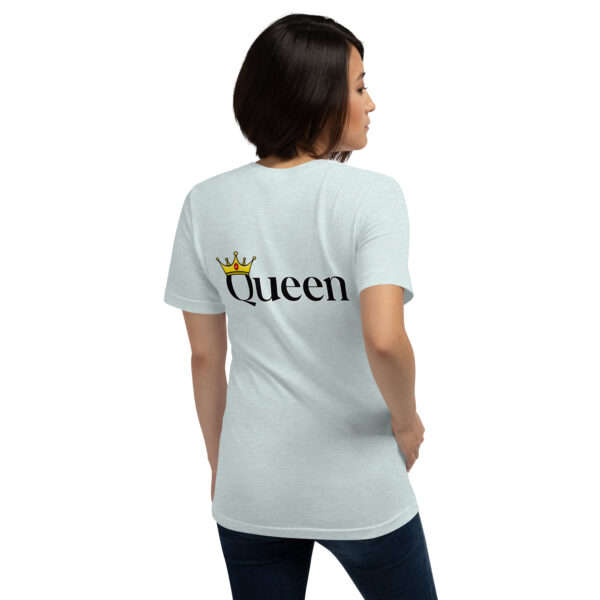 A person wearing a light blue Queen T-shirt, featuring a crown design on the back, is standing and looking to the left.