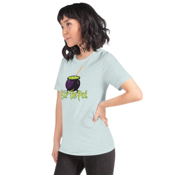 A person in a light blue "Stir The Pot" t-shirt featuring a purple cauldron stands against a plain background.