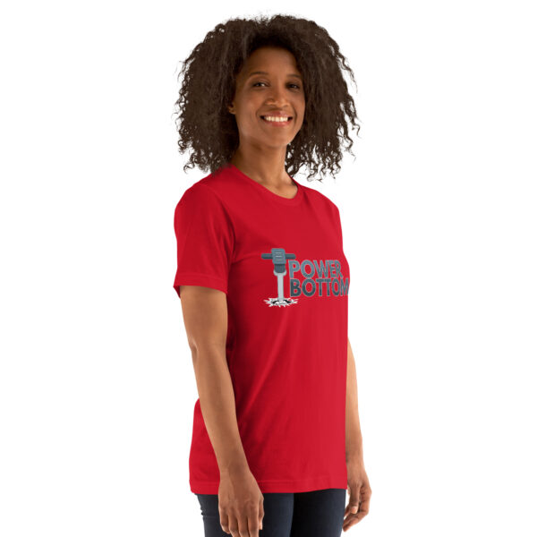 A person with curly hair is standing and smiling while wearing a red t-shirt emblazoned with the "Power Bottom" design.