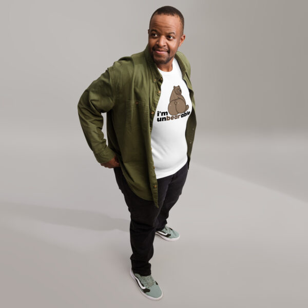 Man in a green jacket and an "I'm Unbearable" graphic t-shirt standing on a white floor, looking to the side.