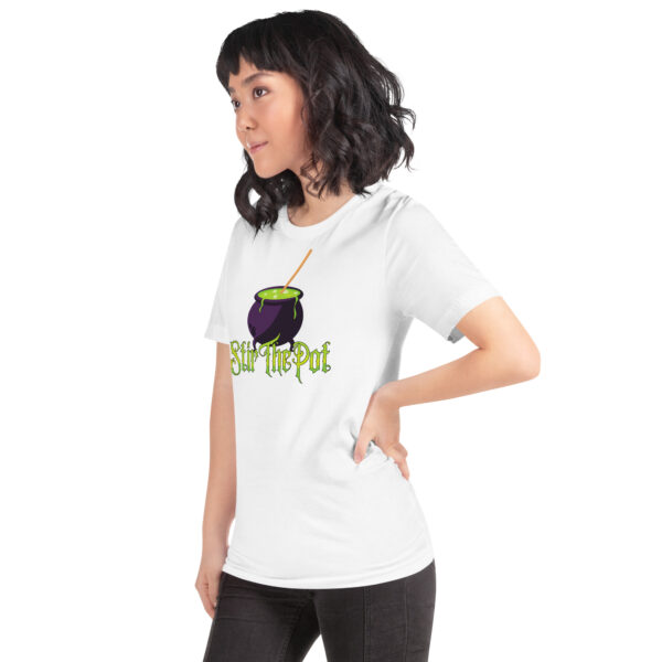 A person is wearing the Stir The Pot white t-shirt featuring a purple cauldron graphic and text, posing sideways with hand on hip.