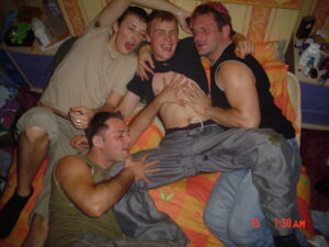 Four roommates are playfully posing together on a bed with orange sheets, laughing and smiling, as they enjoy their shared moments of camaraderie.